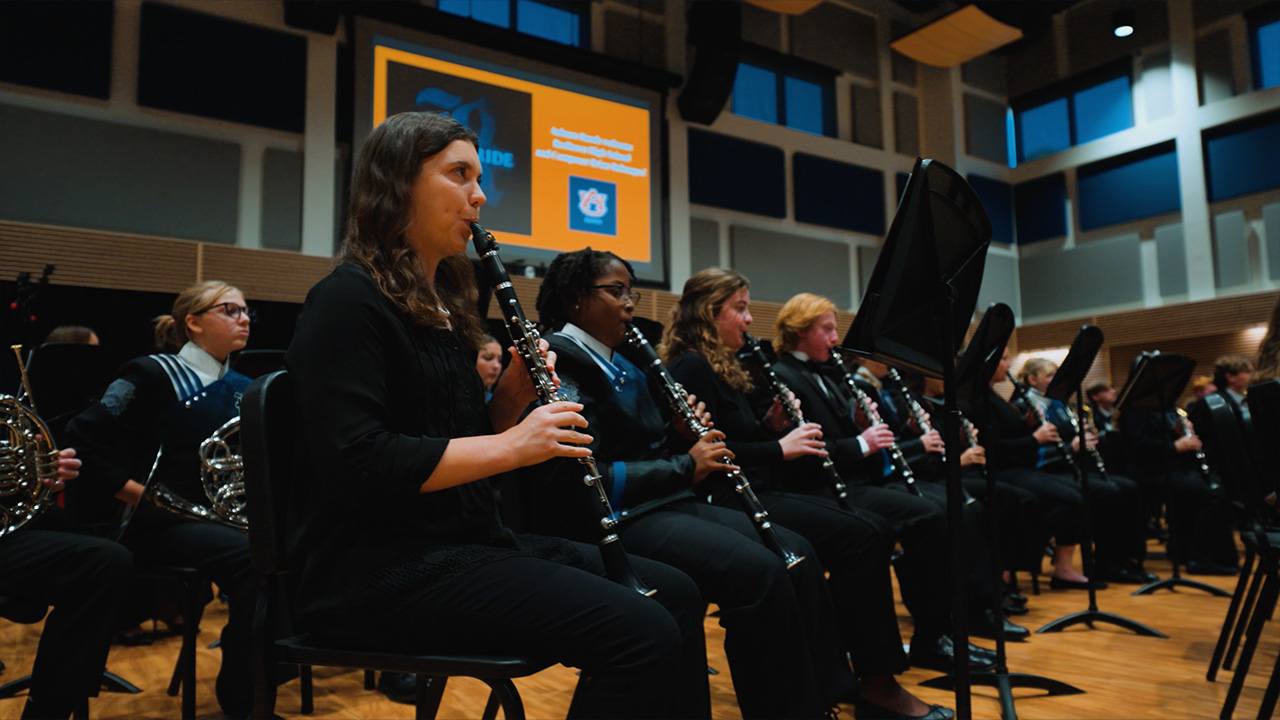 Band members playing clarinets sit in the first row of a symphonic ensemble
