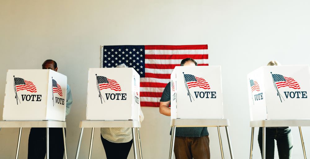 People voting at booths in front of an American flag