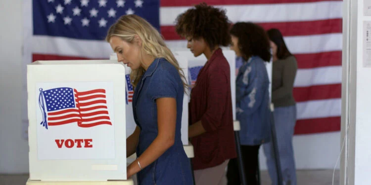 People voting at booths in front of an American flag