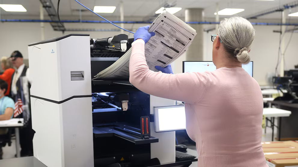 A poll worker feeding a stack of ballots into a machine