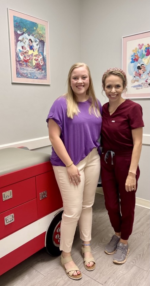 two women, an intern and a doctor, stand together for a picture in an exam room