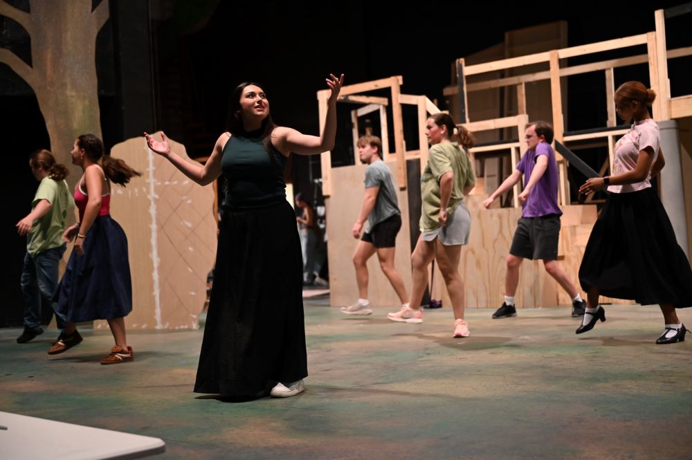Student actor performing on center stage while dancers move across the background