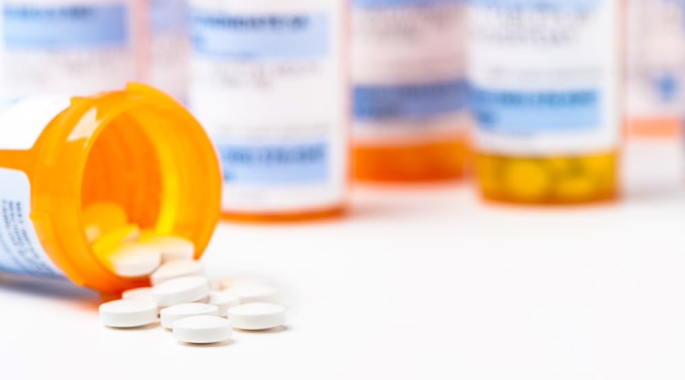 Round white prescription medication pill tablets spilling from a bottle with numerous full bottles in background