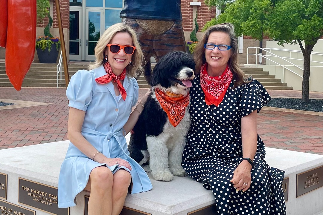 Kay Whaley and Kathryn Hamrick posing for a photo with Sydney the dog on Auburn's campus