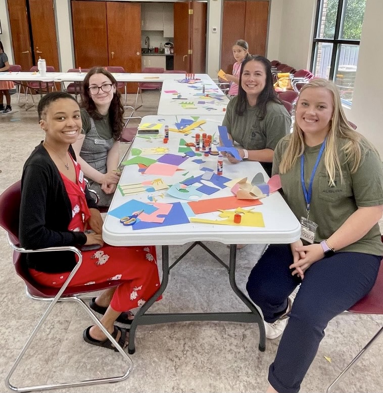 four women sit at a table used to create an arts and crafts project