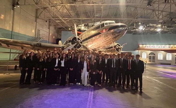 Group of students standing in front of vintage airplane in a large hangar