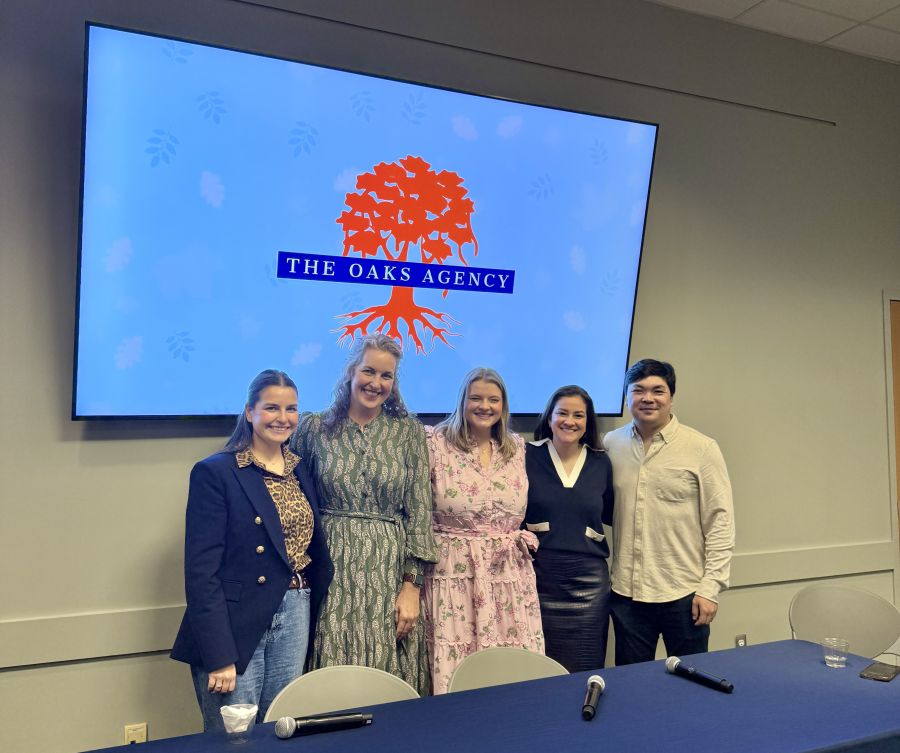 group of people standing in front of a screen with an image of the oaks agency logo