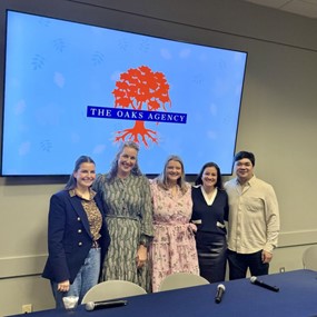 group of people standing in front of a screen with an image of the oaks agency logo
