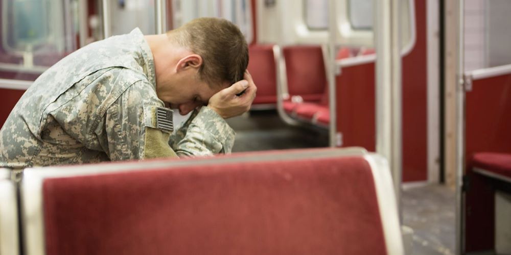 A man in military uniform holds his head in his hands on an empty bus