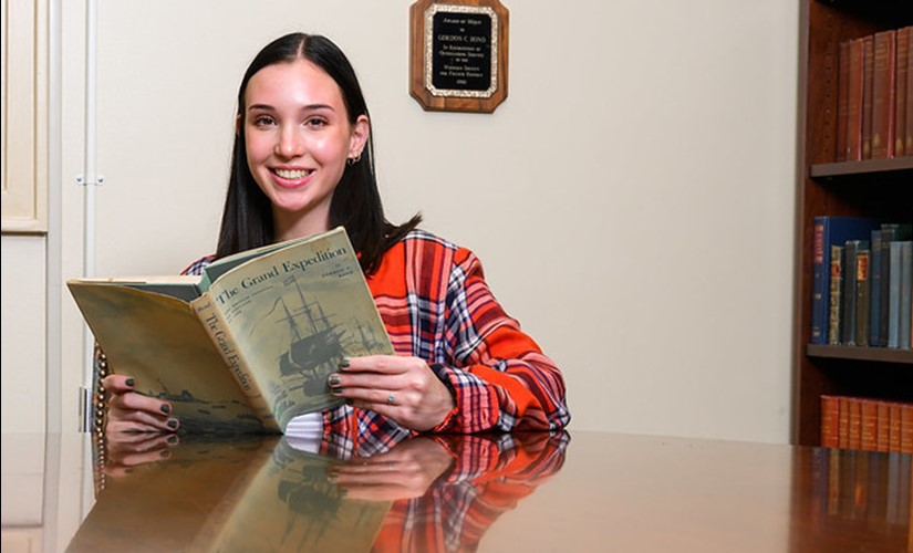 Emma Bond reads The Grand Expedition, a book written by her grandfather, inside the Gordon Crews Bond library