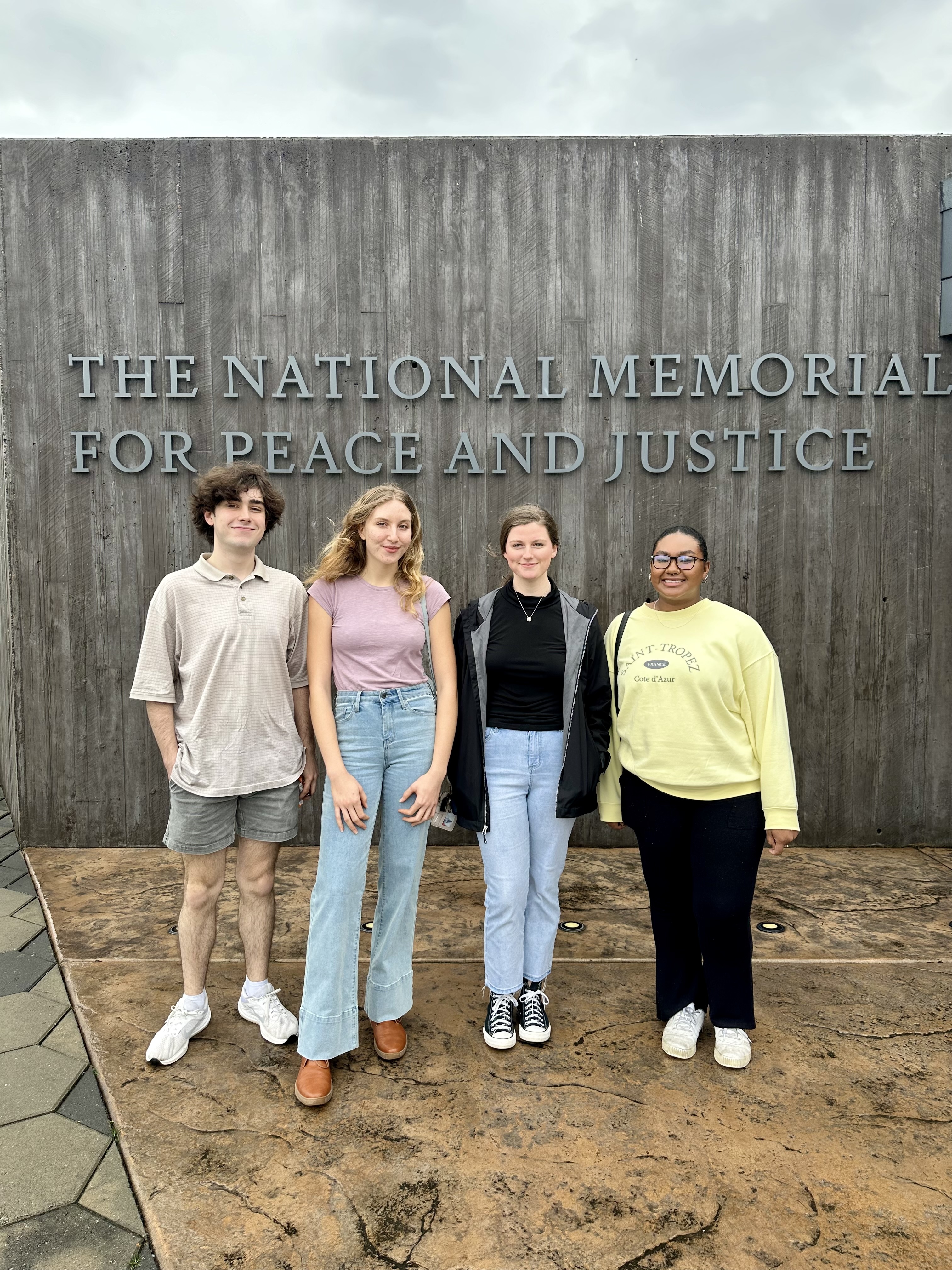 Four Living Democracy students stand in front of a sign at the entrance of the National Memorial for Peace and Justice in Montgomery