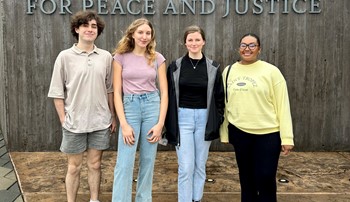 Four Living Democracy students stand in front of a sign at the entrance of the National Memorial for Peace and Justice in Montgomery