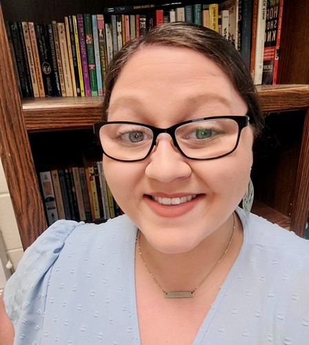 Former Fruitdale High School student, Ashley Booth, smiles in front of library shelves