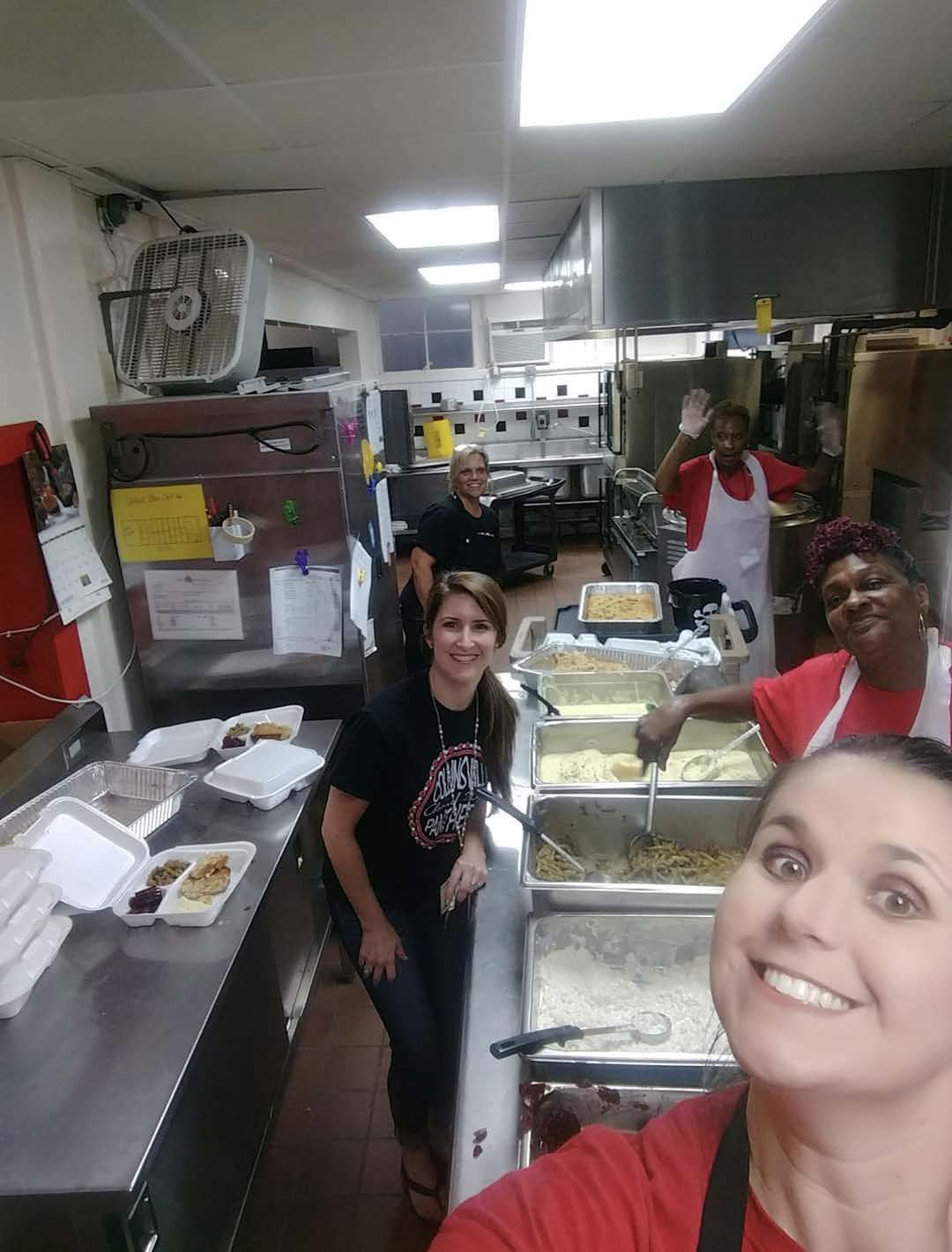 Group of people standing in a school kitchen smiling at camera