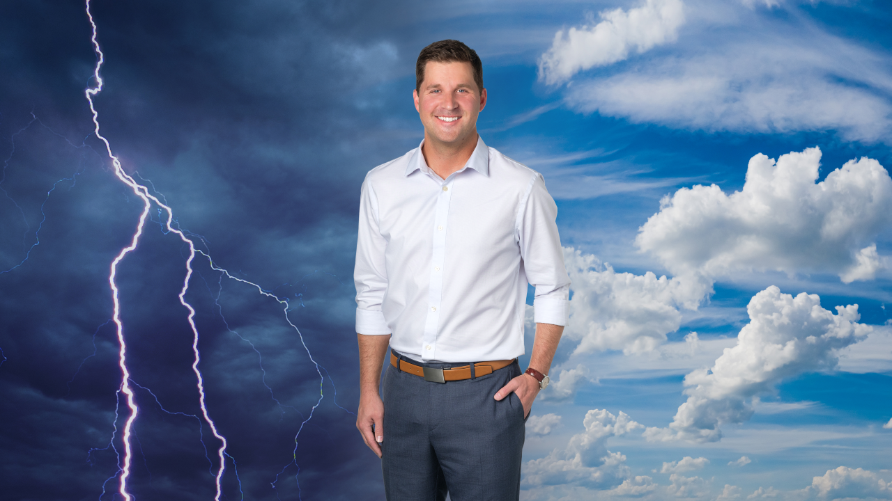 Stephen Neslage posing for photo. On his left, a thunderstorm darkens the sky. On his right, clouds drift across a blue sky.