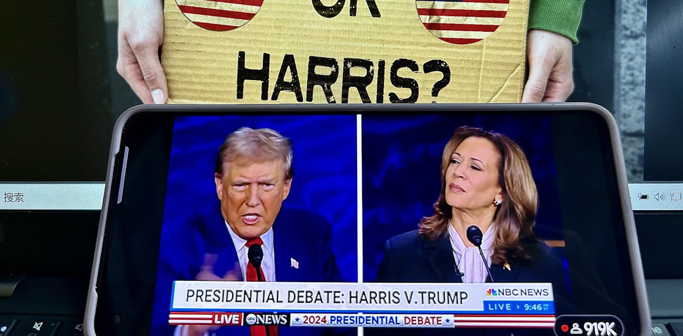 Phone showing a split screen of the 2024 Presidential debate with a campaign sign in the background