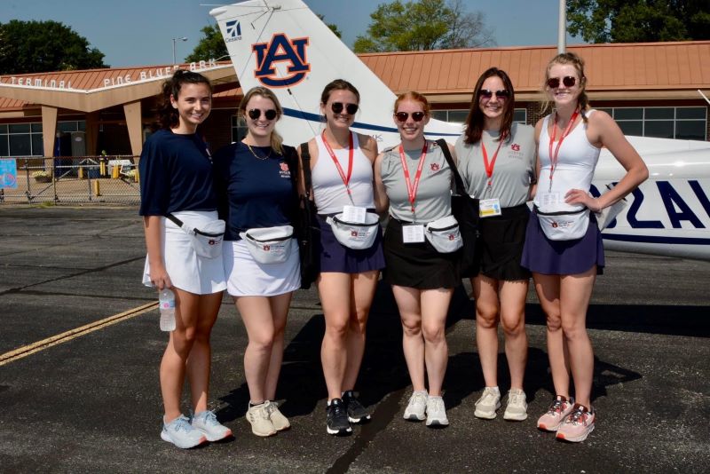 The War Eagle Women stand in front of an Auburn airplane at the airport