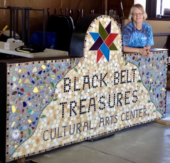 Linda Muñoz, a glass mosaic artist in North Alabama, stands with Black Belt Treasures' sign