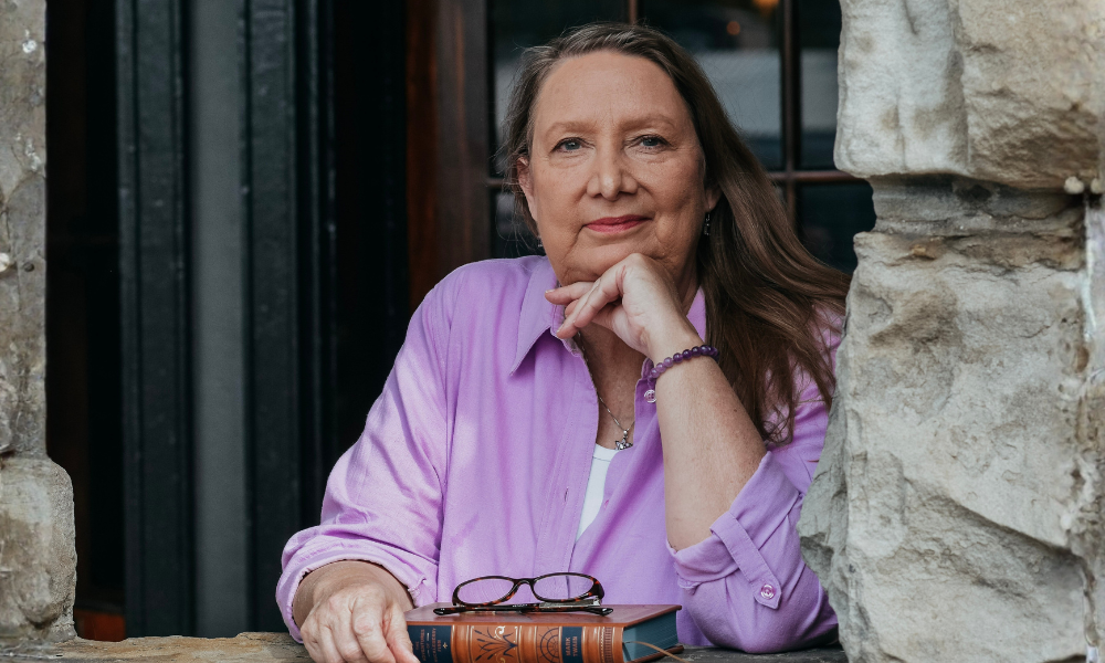 Leslie Harper Worthington poses in a stone window frame with her glasses and a book