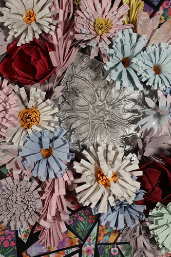 Detail image of the 2025 Dean's Choice Purchase Award-winning artwork, "Rebirth" by student Mia Williams. Flowers made of handmade paper and a cast iron relief of a stylized flower overlap on top of a collage of handmade paper.