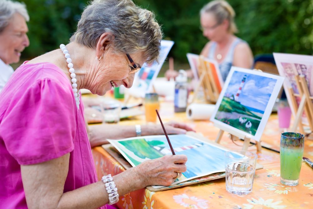 An older woman smiling as she paints with a group