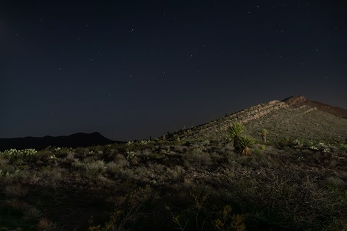 Photograph by Marni Shindelman depicting a desert hillside at night. The hill is brightly lit.
