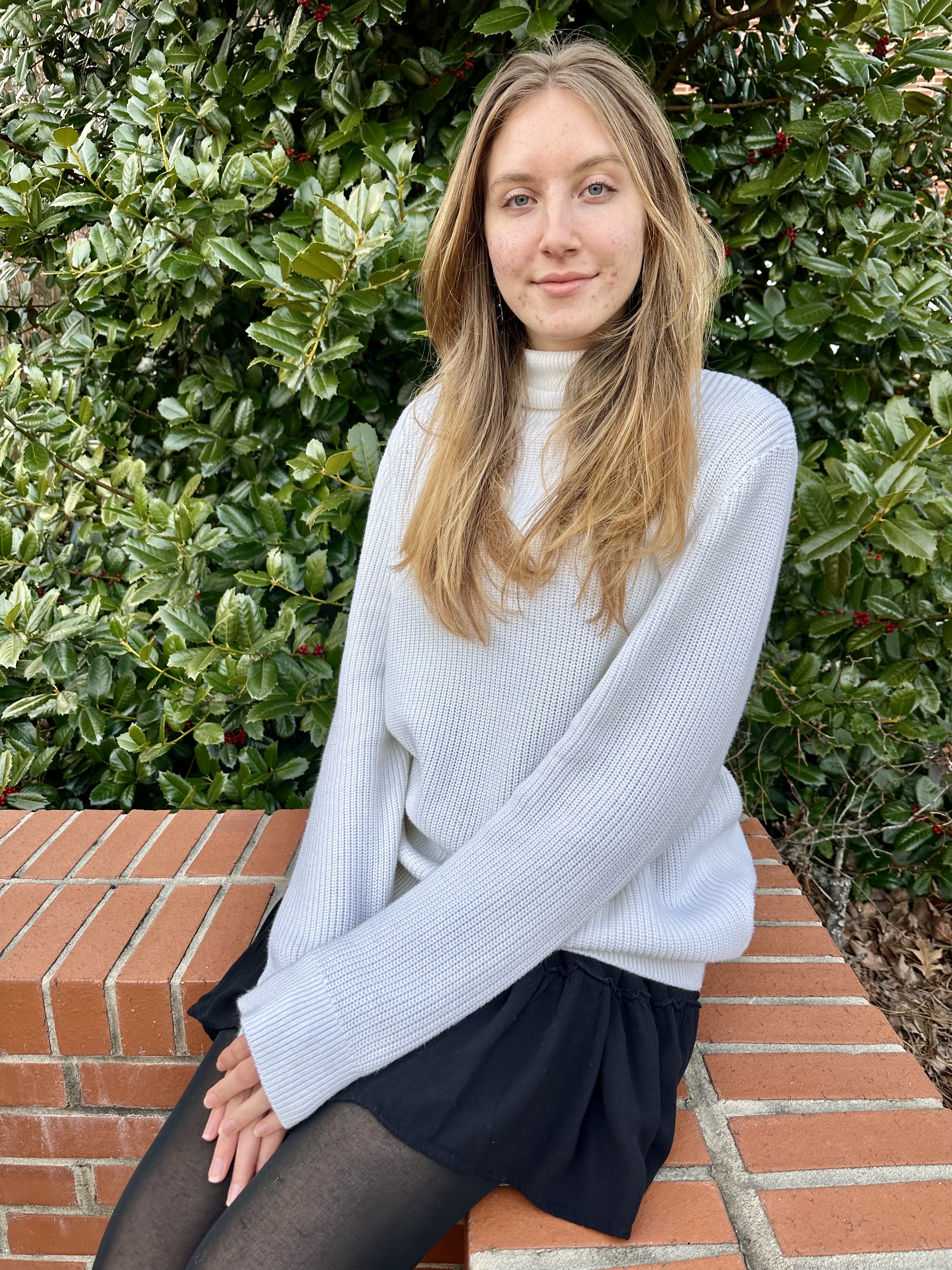 Colette Whitney sits on a brick wall in front of shrubs