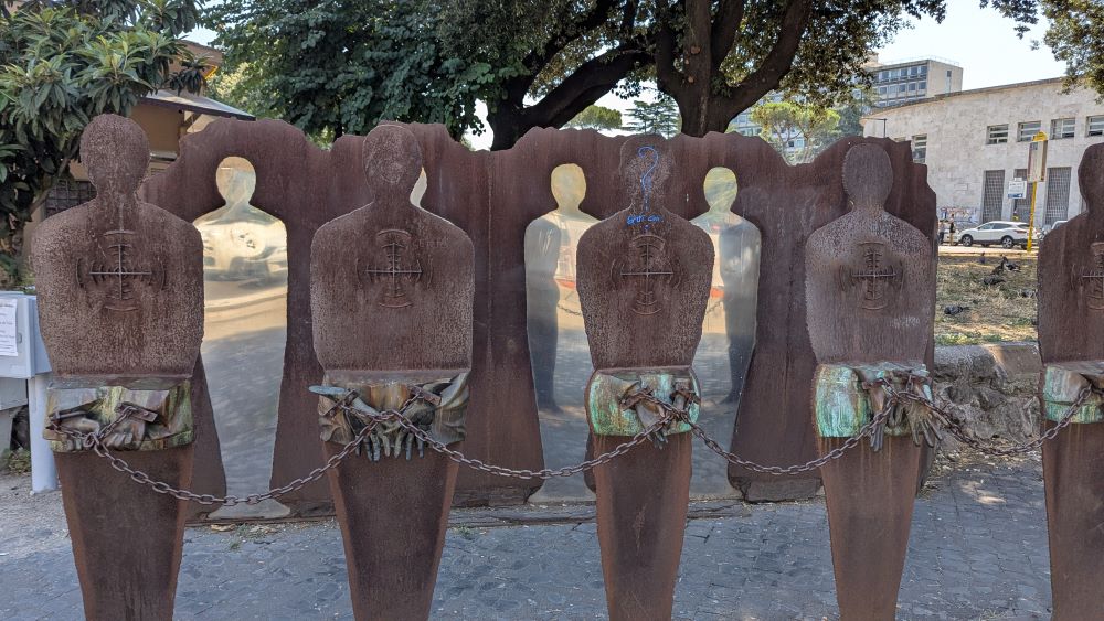 A monument to those who resisted Fascism, including metallic silhouettes with chains on their hands and targets on their backs