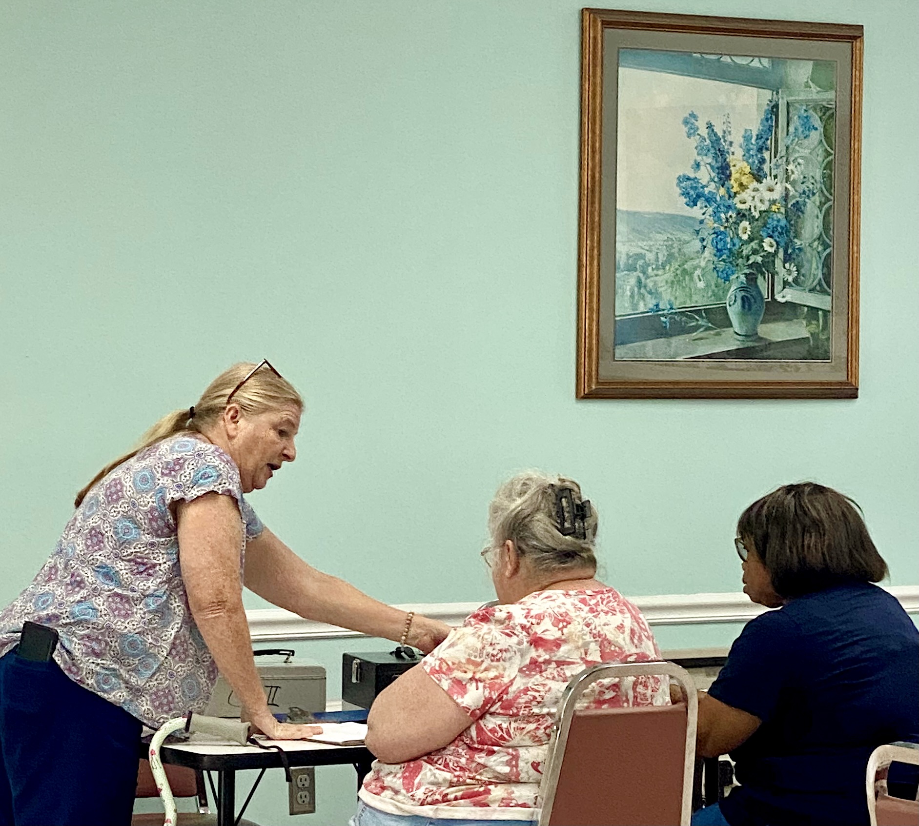 woman standing talking to two women sitting at a table.