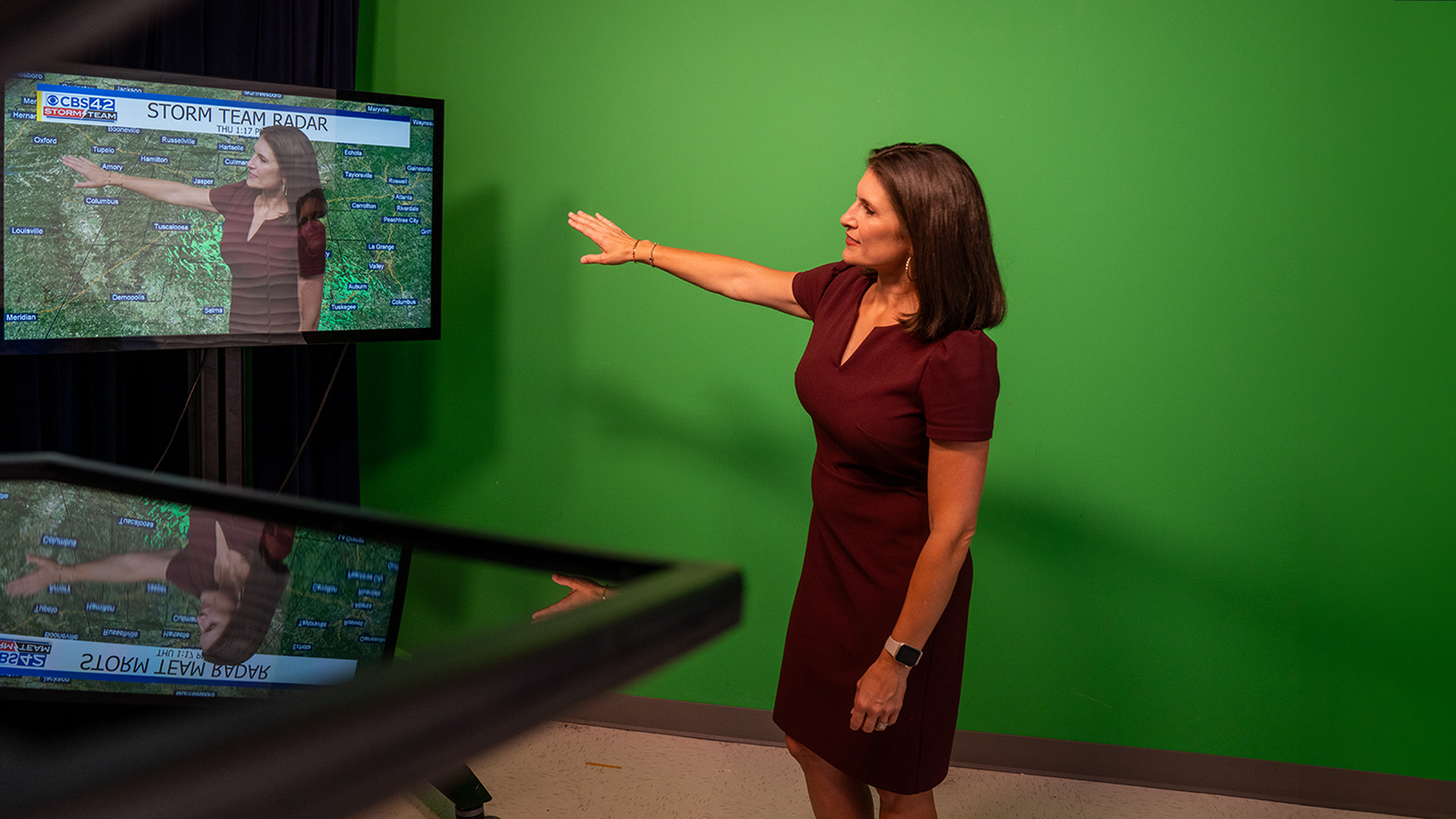 Ashley Gann pointing to weather map in front of a green screen