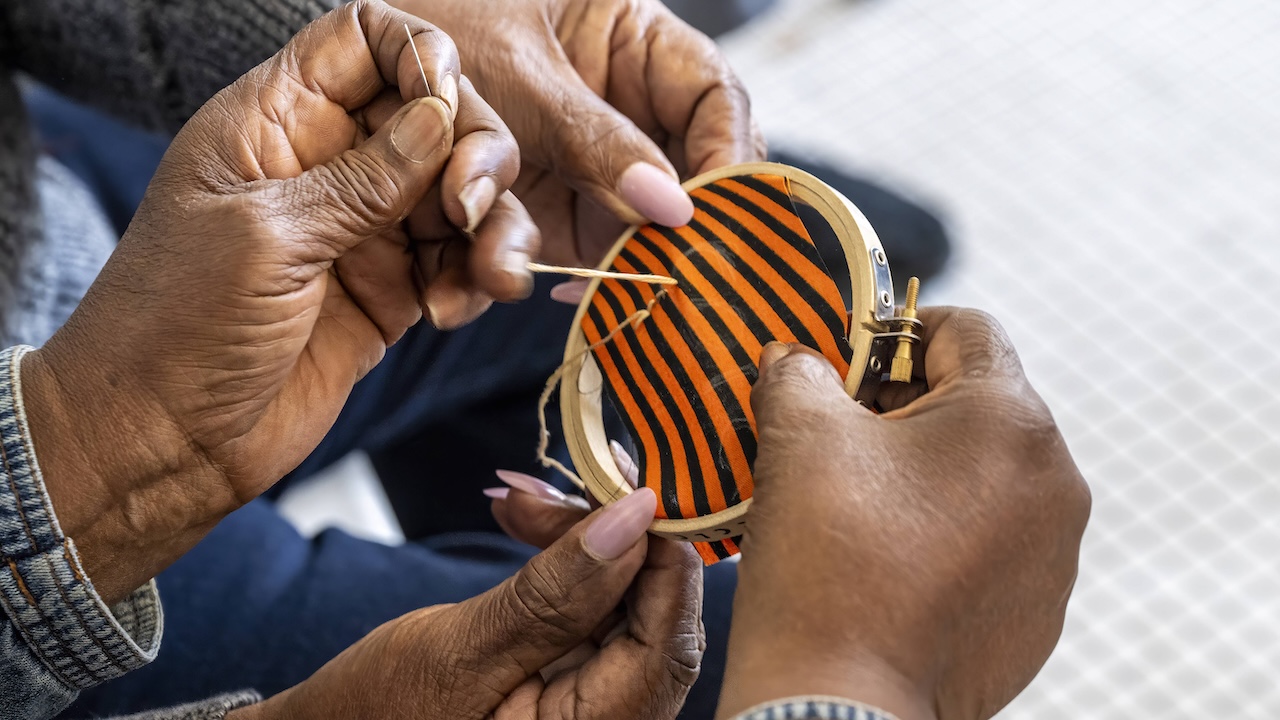 Hands stitch a name into quilting fabric squares
