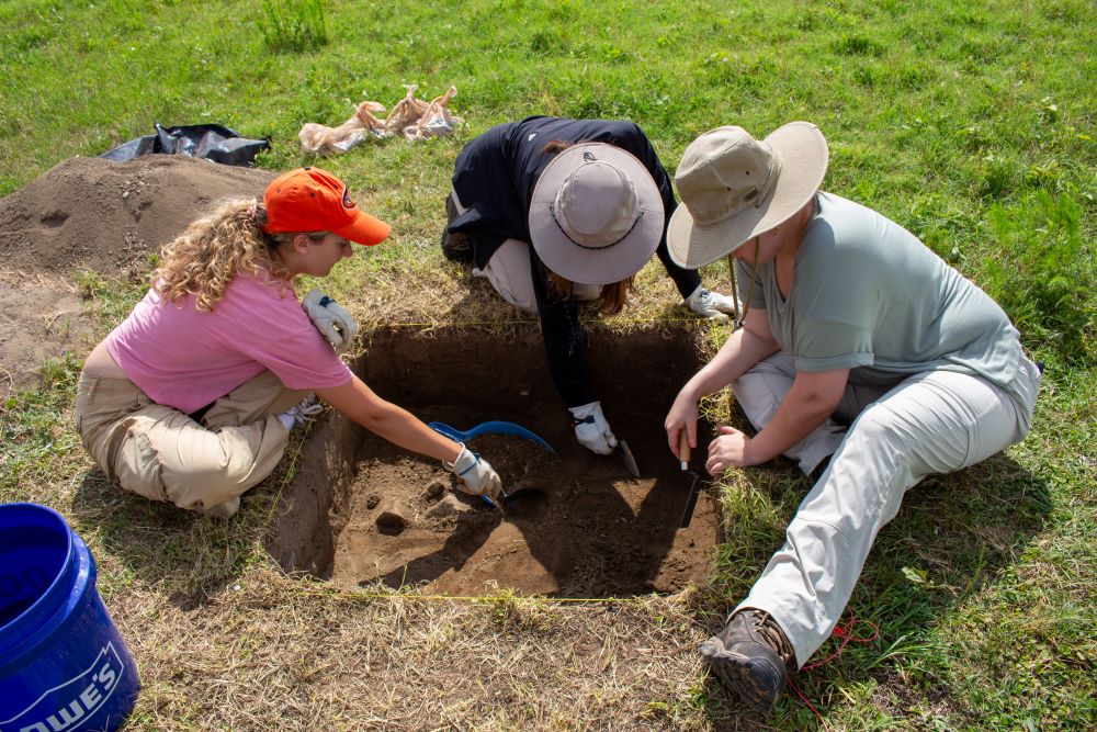 Students gathered around hole in the ground looking for artifacts