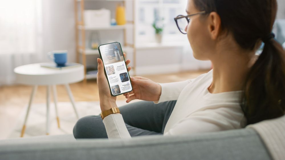A woman sitting on her couch reading news on her phone