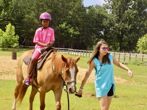 a young woman guides a girl atop a horse around a riding ring