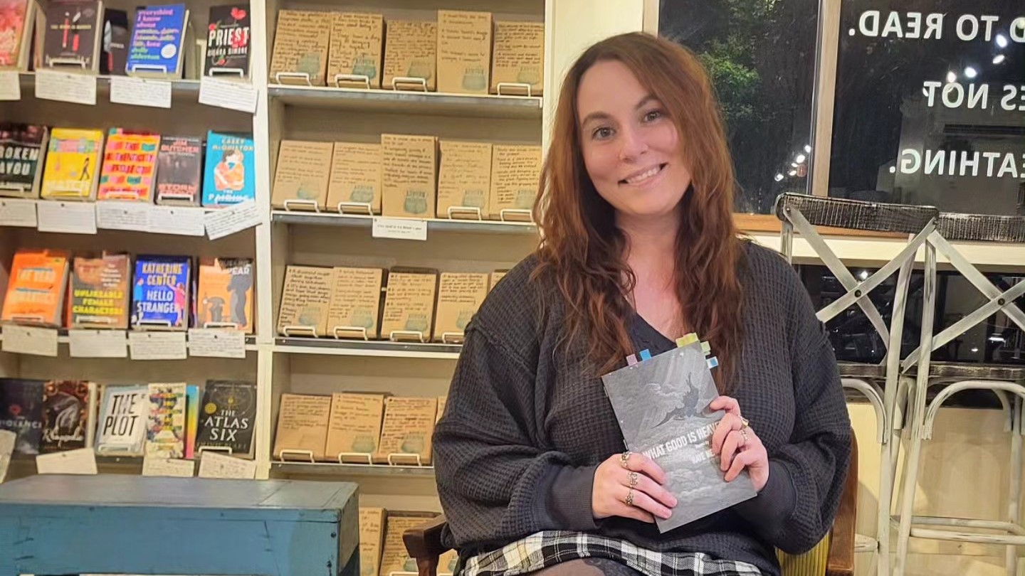 Raye Hendrix holding "What Good is Heaven" at an Auburn bookstore