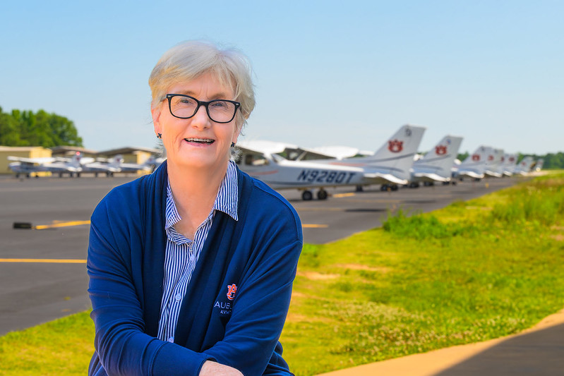 Jill Glidewell smiling for a photo on a sunny day at the Auburn airport in front of the Auburn aircraft fleet
