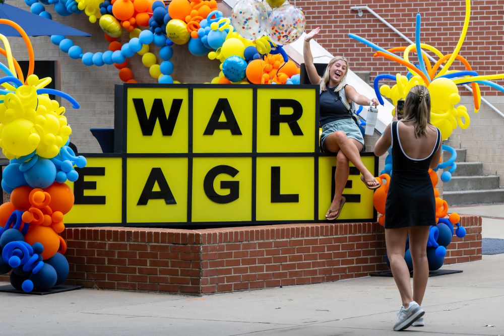 Students taking photos at a large War Eagle sign during a first week of class celebration