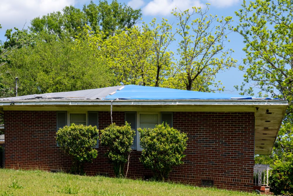 Blue tarp covering roof of a small brick house