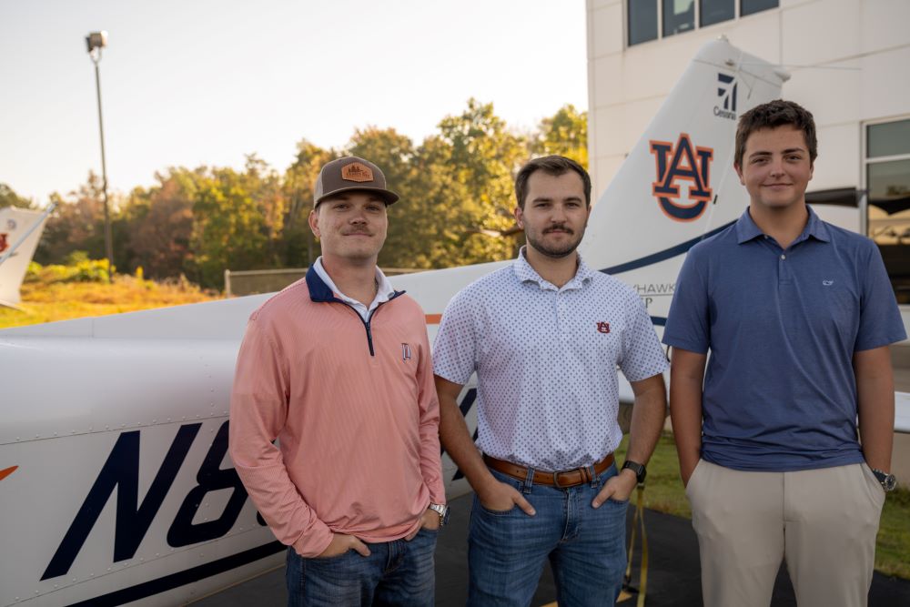 Nick Reyzin, Noah Henry and William Abbott posing for photo in front of an Auburn airplane