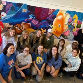 art students posed in front of colorful mural