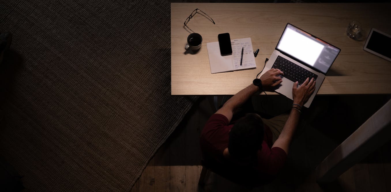 Person sits at a desk answering emails by the light of a lamp in a dark room