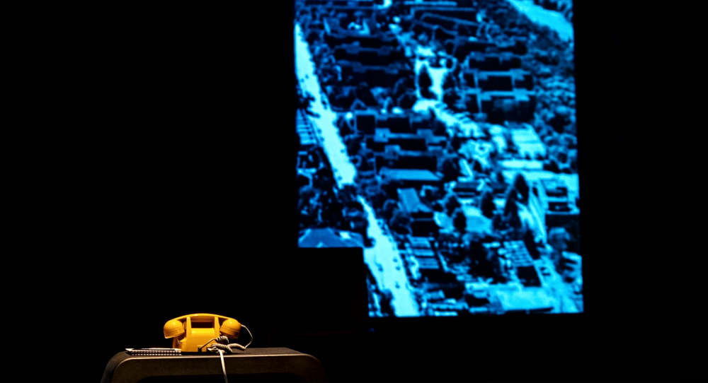 Yellow telephone sitting on stage in front of a blue background during Jitney