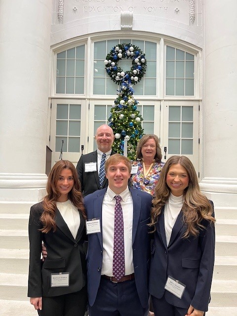 students and faculty posing for a photo in front of a large glass door